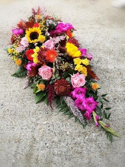 rustic funeral Teardrop spray to include sunflowers, heather, pink roses, cerise gladioli, red blooms.