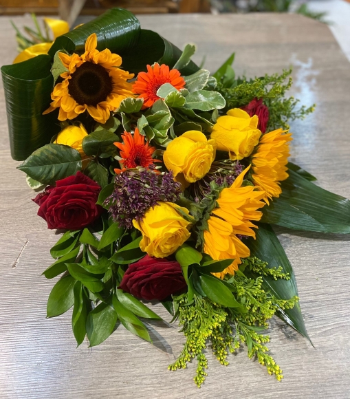 This summer vibe sheaf is a mix with Sunflowers, orange daisies, Red Roses and seasonal alium, solidago. By Blooms and Candy Florist