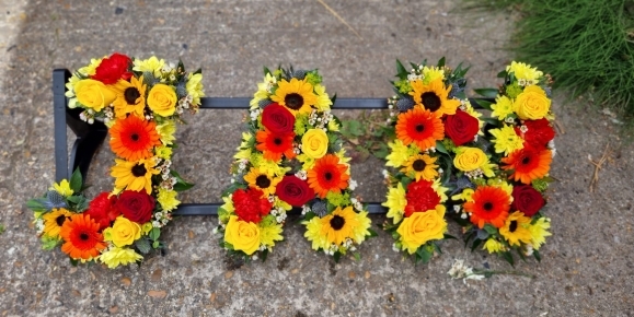 Mixed bright funeral flowers to include sunflowers and roses and fillers designed by florist in Hayes,  Bromley 