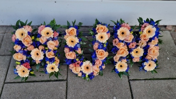 Mix of peach roses and gerberas with blue delphinium and thistle with greenery. By Blooms and Candy Funeral Florist Bromley