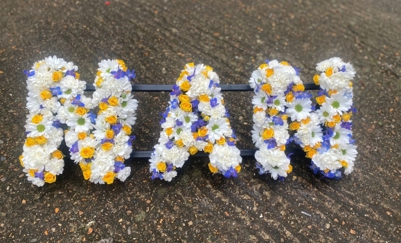 A delicate mix of white daisies, carnations with spray yellow roses and light blue delphiniums. By Blooms and Candy funeral florist Bromley